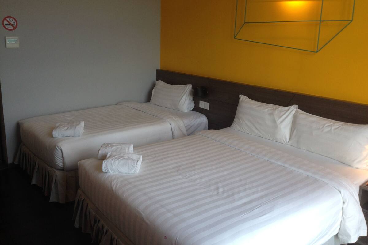 Een hotelkamer met twee bedden, elk voorzien van witte lakens en kussens, een hoofdeinde en een wandlamp.