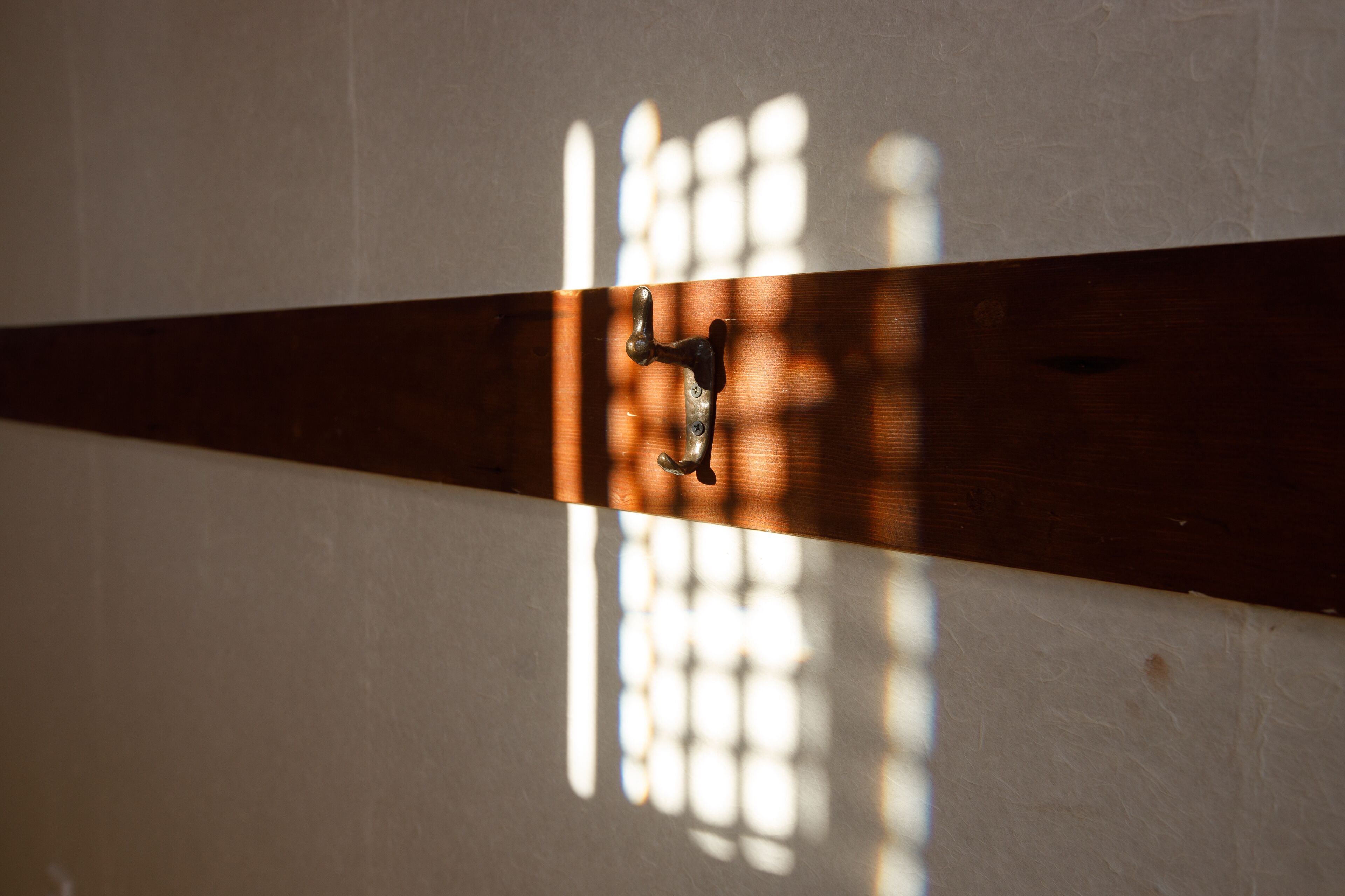 A wooden beam with a metal fixture, sunlight casting shadows on a wall.
