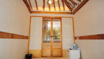 Una habitación tradicional japonesa con vigas de madera, un puertas correderas, un refrigerador pequeño y un cubo de basura negro.