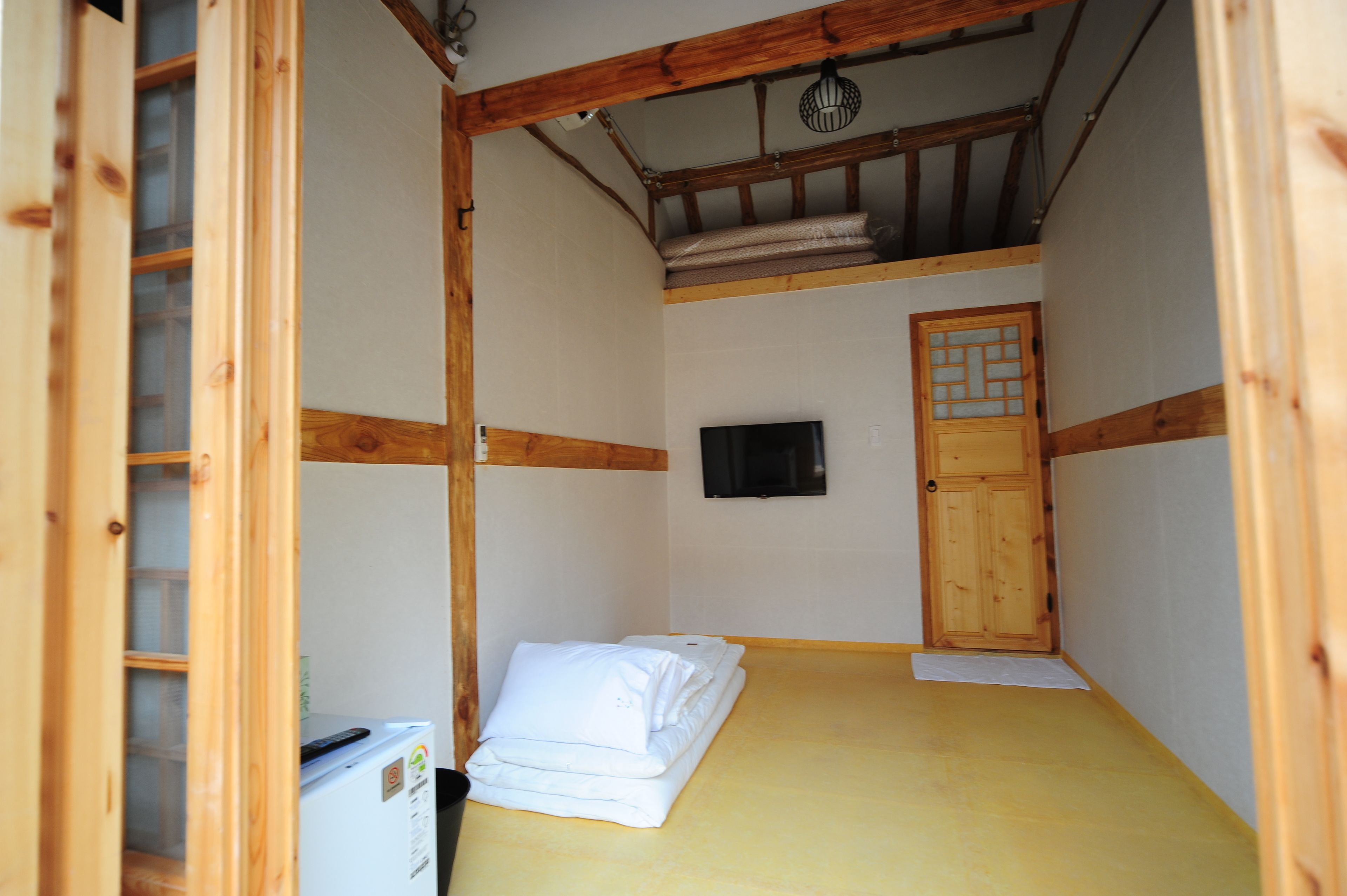 A compact room with a bed, a television, and a wooden door.