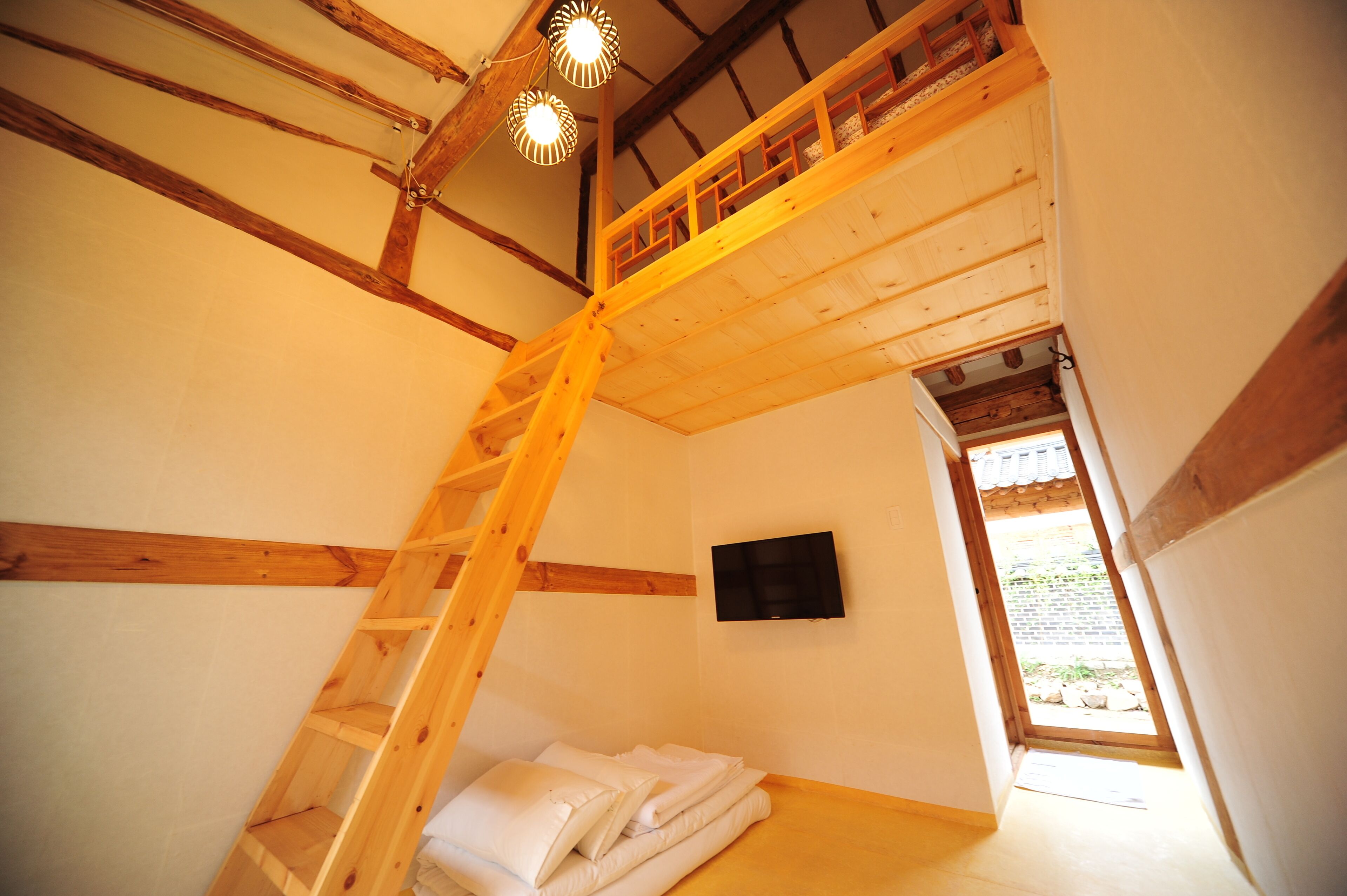 A room with a wooden ladder leading to a loft area, a flat-screen TV mounted on the wall, and a door leading to an outdoor area.