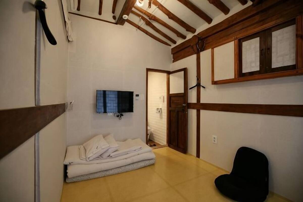 A room with a bed, a black chair, a television, and a wooden ceiling.