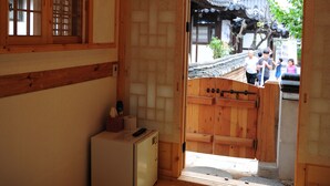 A traditional Japanese room with tatami flooring, a low wooden bed, a small refrigerator, and a view of a traditional courtyard. - Gaeunchae (Jeonju)