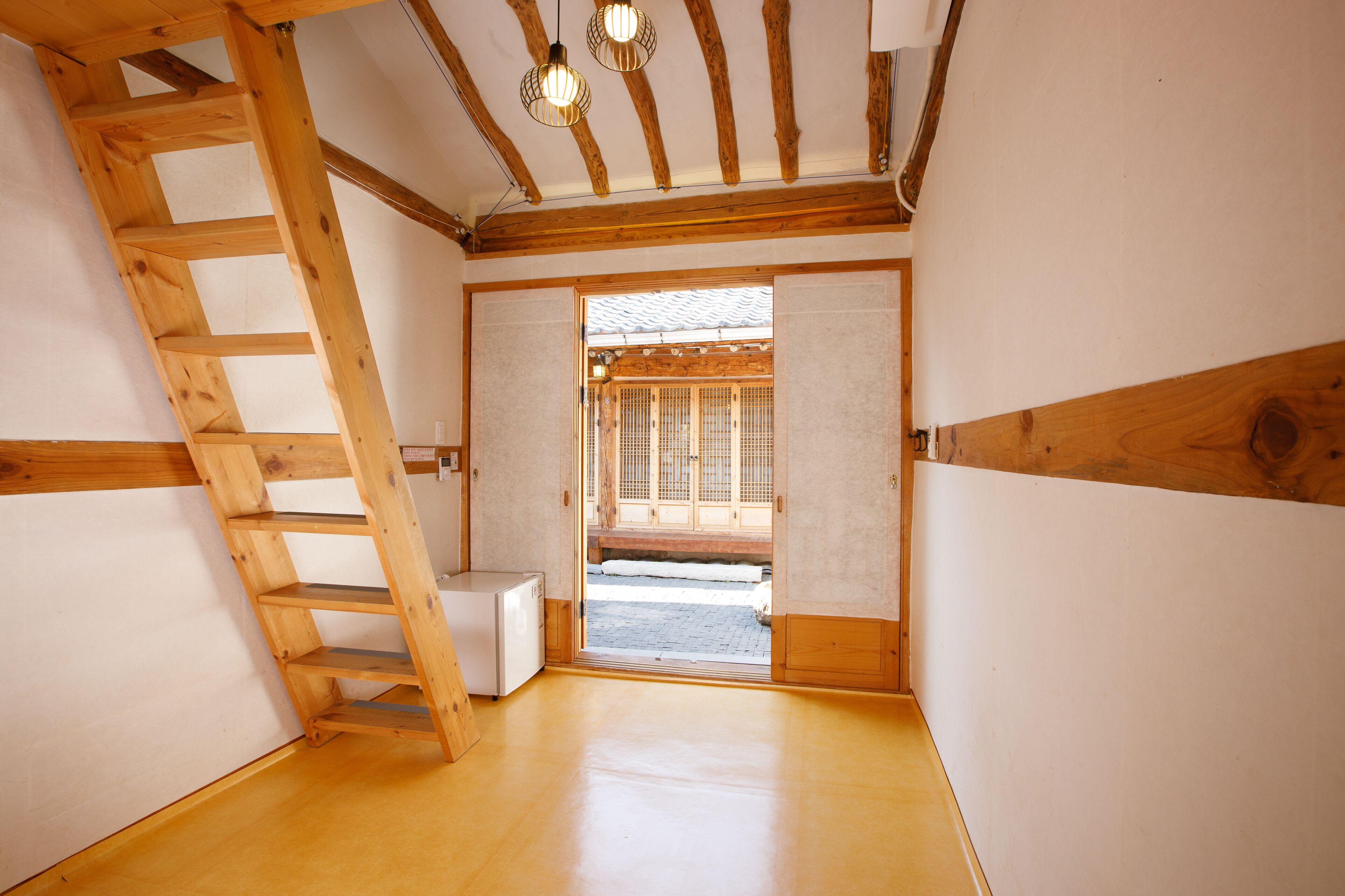 A room with a wooden ladder, a small white cabinet, and a sliding door leading to an outdoor area with a wooden structure.