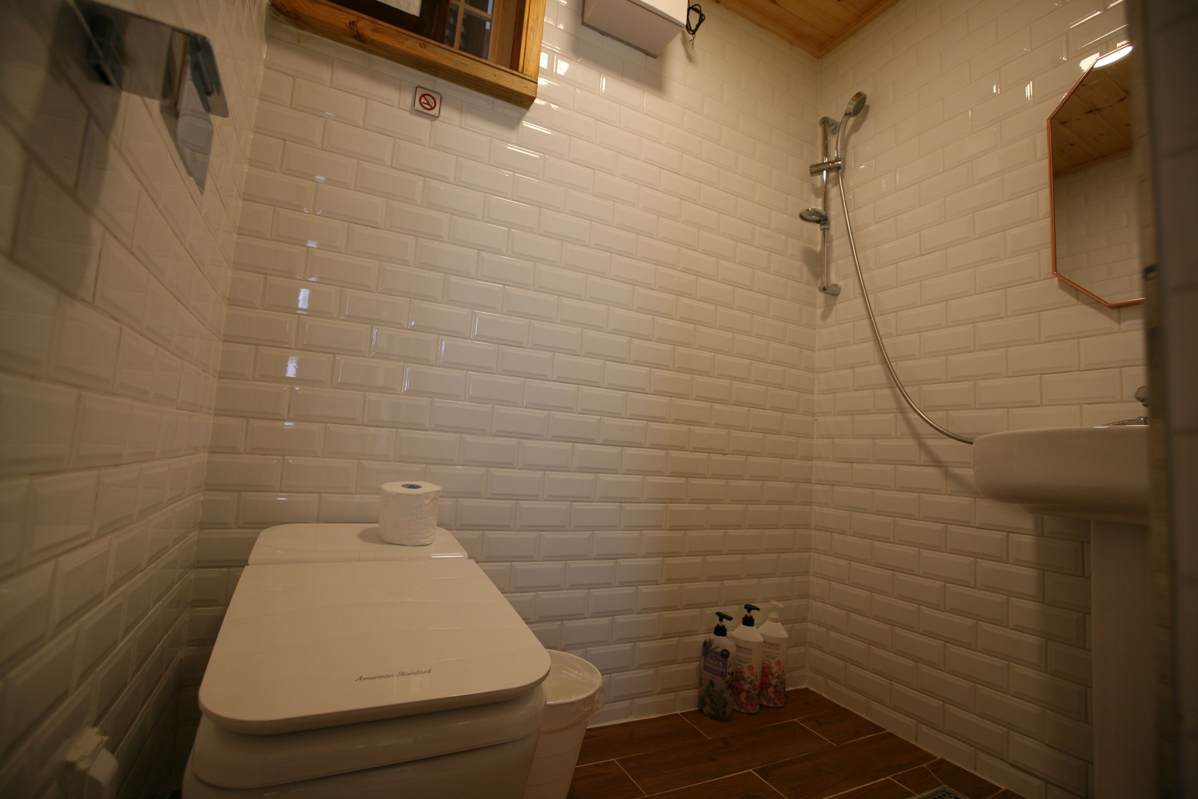 A bathroom with white subway tiles, a toilet, a shower with a handheld showerhead, and a mirror.