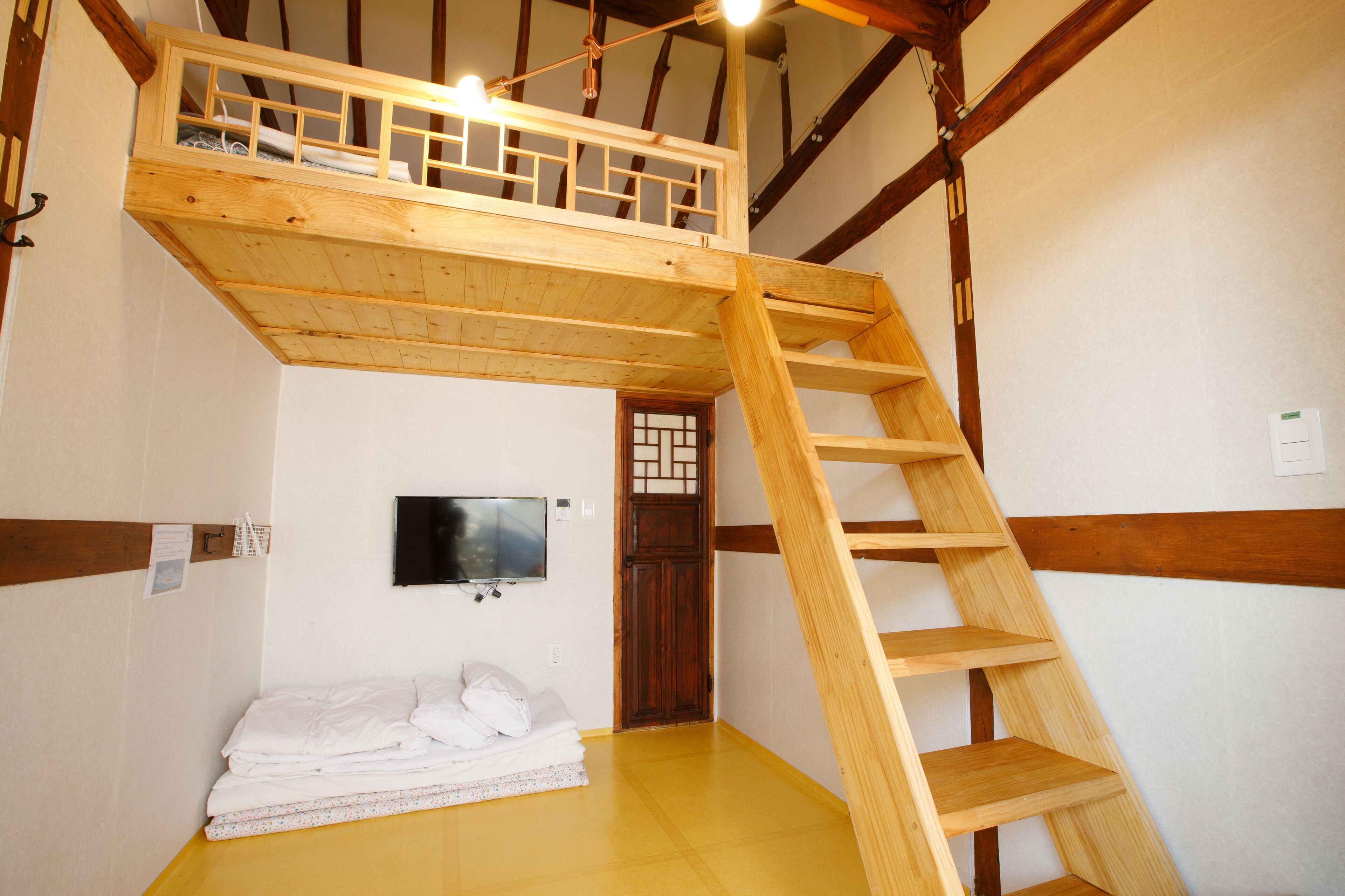 A room with a wooden loft bed, a wooden ladder, a television on the wall, and a traditional Japanese door.