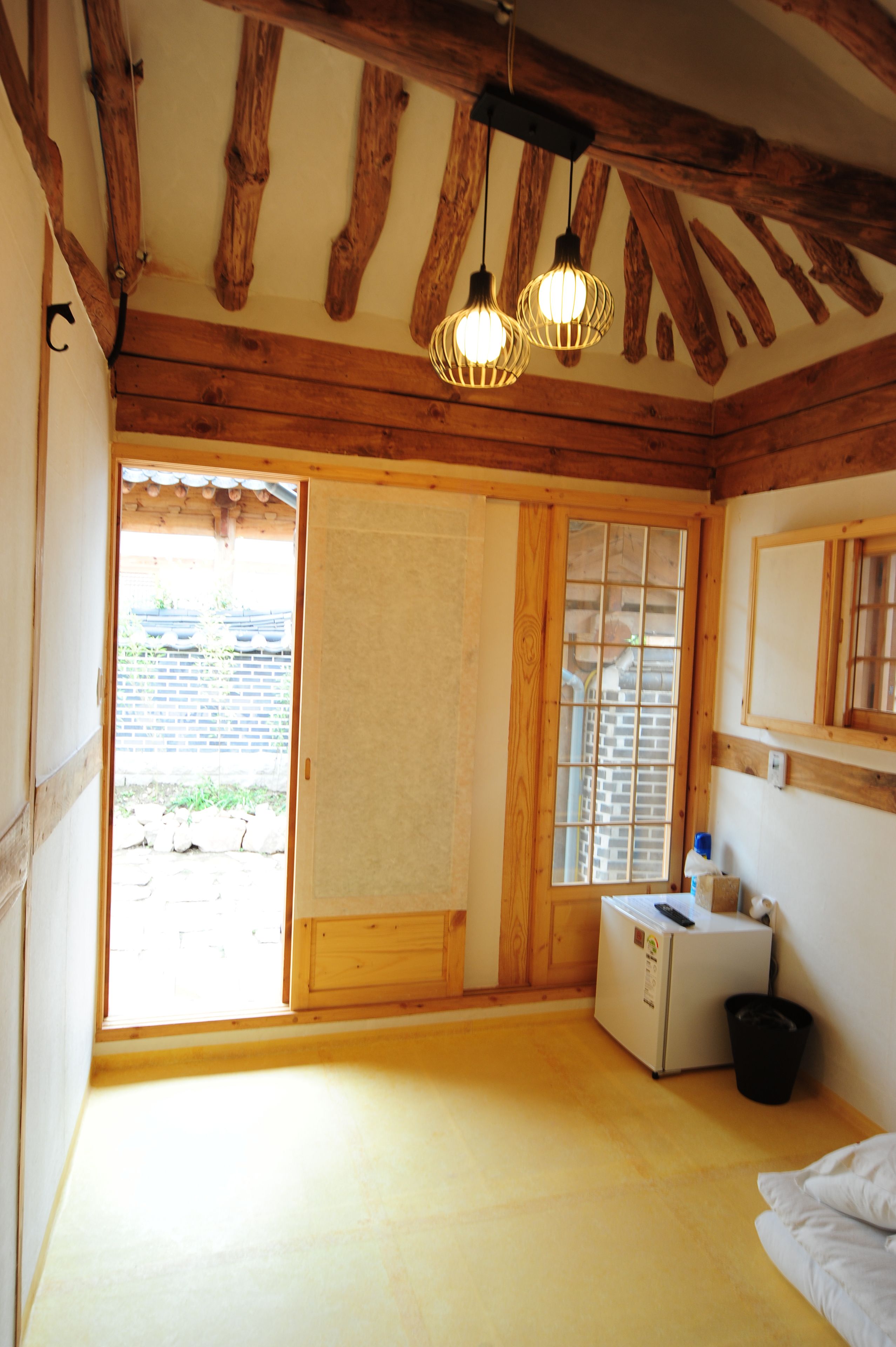 Una habitación con vigas de madera, un refrigerador, una ventana y una puerta que da al exterior.