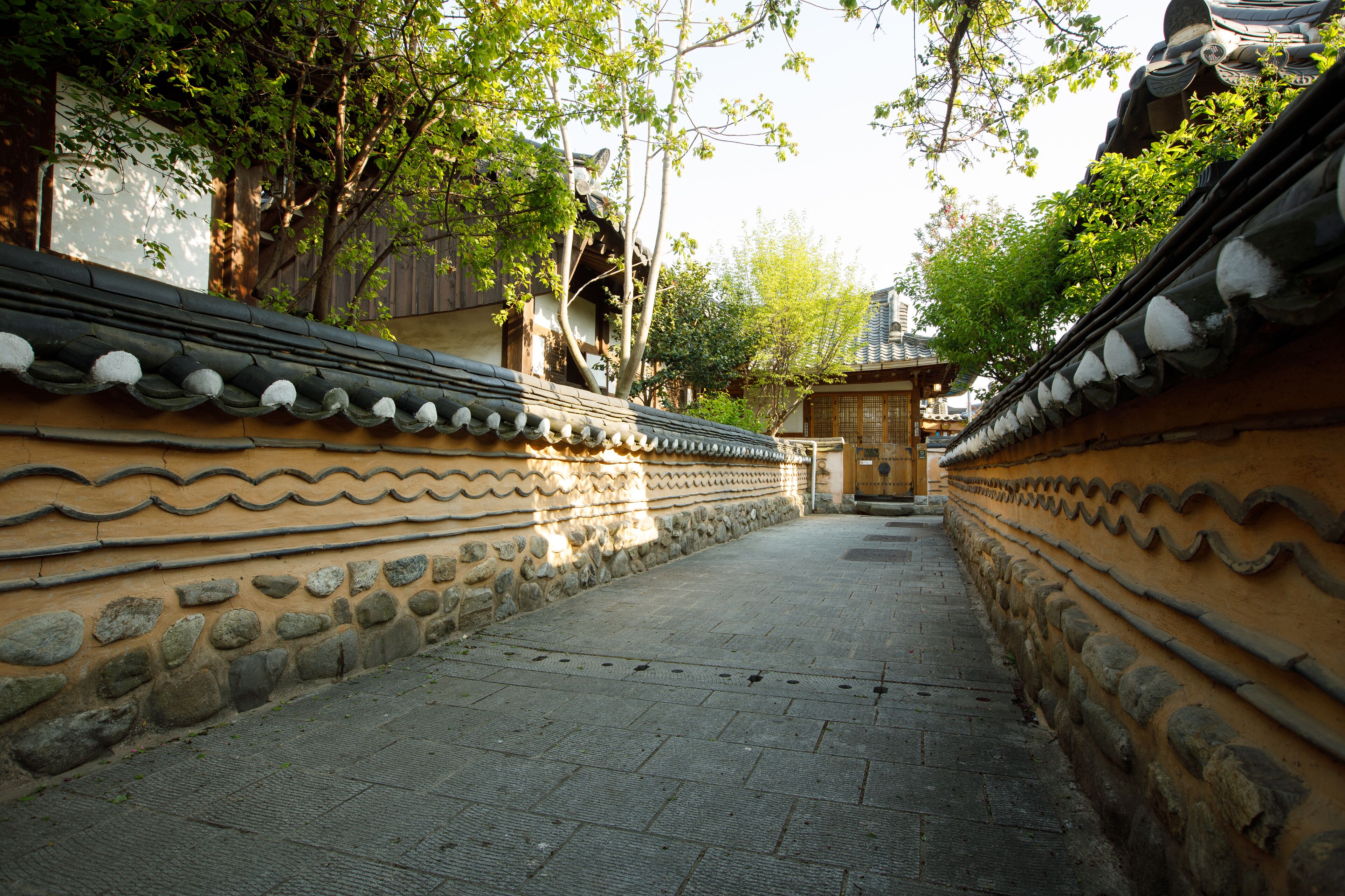 A traditional pathway flanked by stone walls with decorative patterns, leading to a traditional building with a tiled roof.