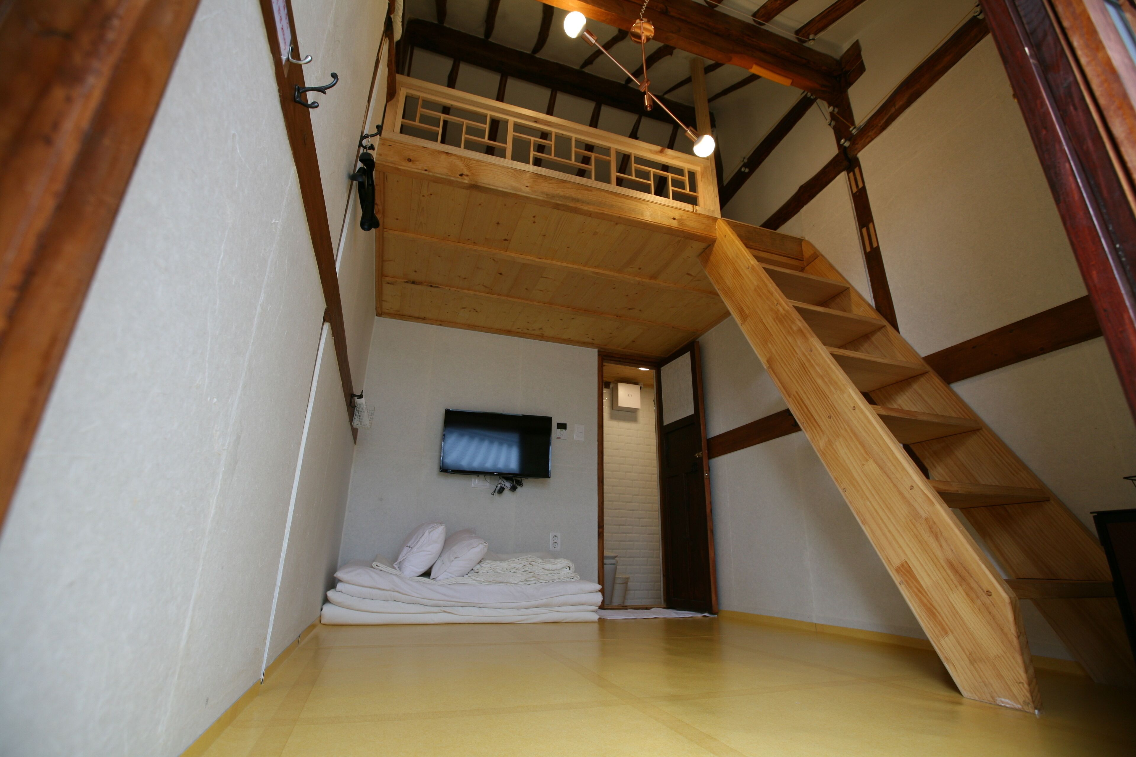 Une pièce avec un lit en hauteur en bois, un téléviseur fixé au mur et un escalier menant à la mezzanine.