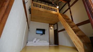 Une pièce avec un lit en hauteur en bois, un téléviseur fixé au mur et un escalier menant à la mezzanine.