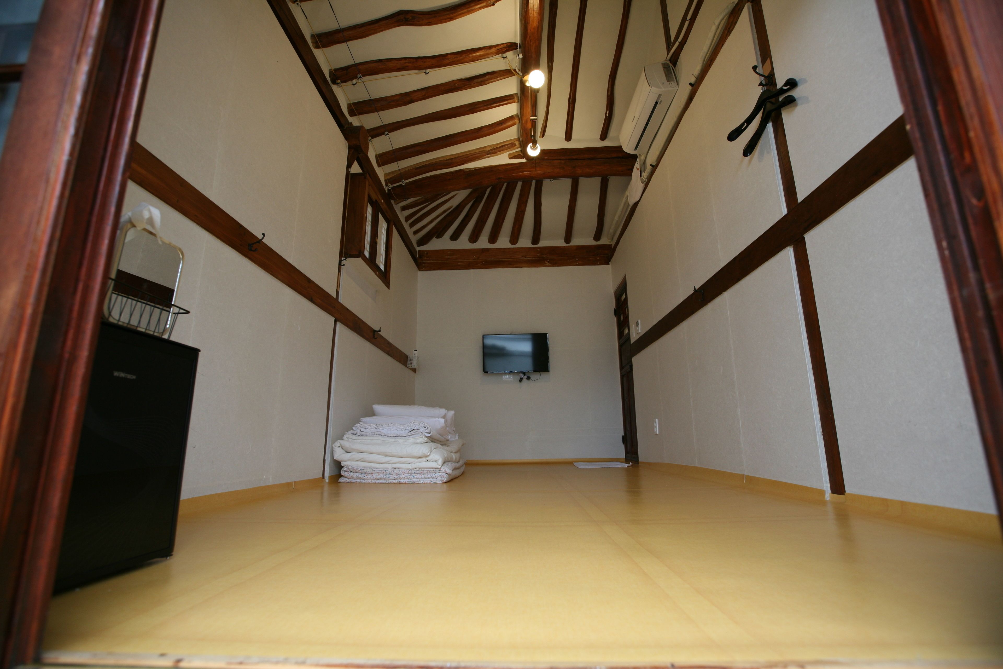 Une pièce avec un plafond en bois, un téléviseur à écran plat fixé au mur et une pile de serviettes pliées appuyées contre le mur.