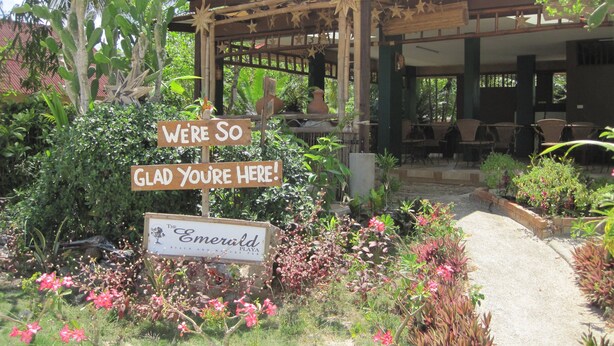 Ein Gartenbereich mit einem Holzschild, auf dem steht: 'WE'RE SO GLAD YOU'RE HERE!' und 'The Emerald Beach and Nature Park'.