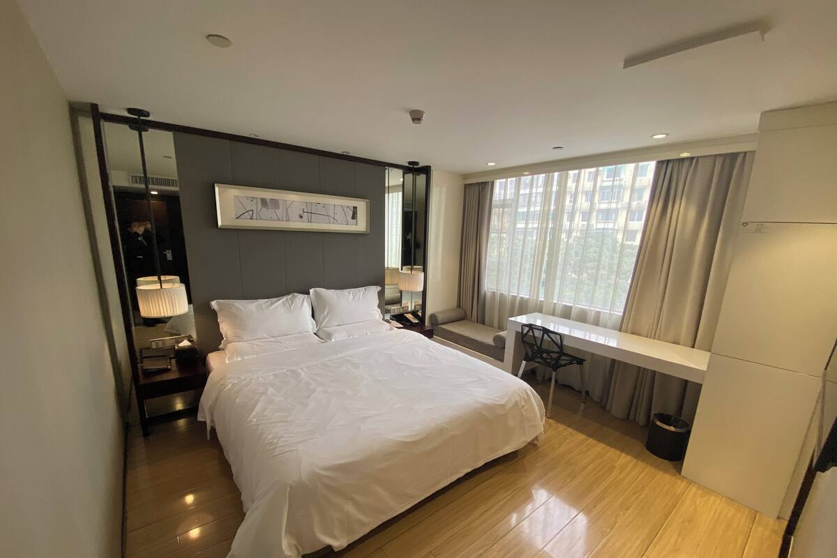 A modern hotel room with a large bed, a desk, and a window with curtains.