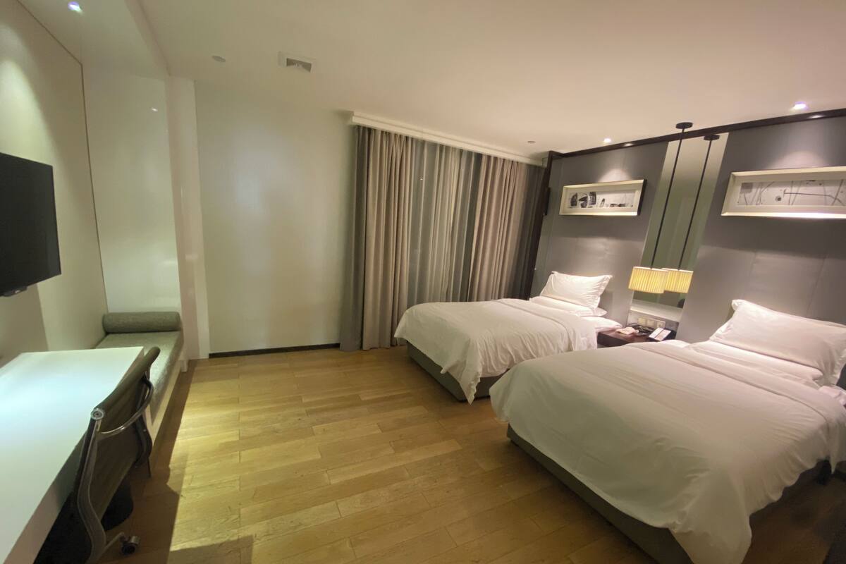 A hotel room with two beds, a desk, a chair, a TV, and a window with curtains.