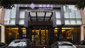 La entrada del Hotel City Join, con fachada de vidrio, un acceso cubierto y dos coches estacionados en frente.