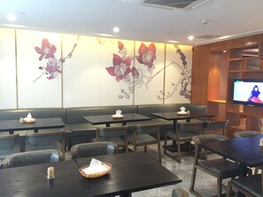 Un restaurante con cabinas y mesas, una pantalla de televisión y decoración floral en las paredes.