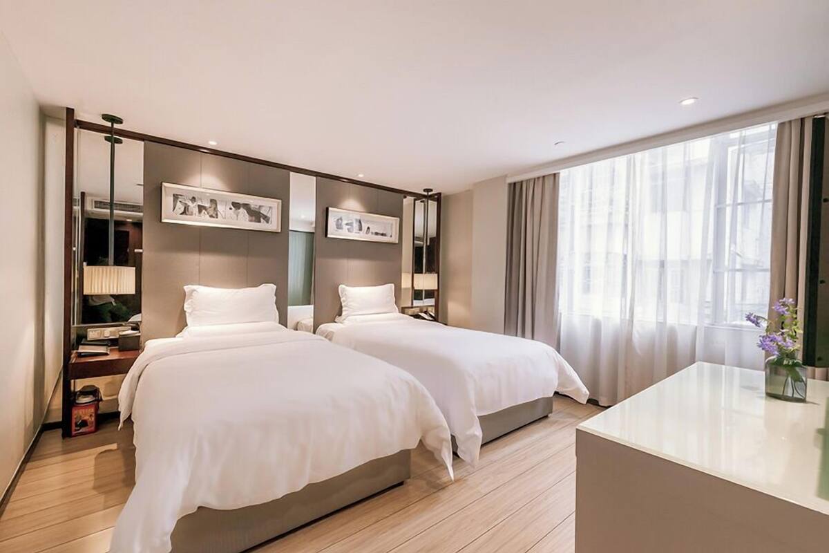 A modern hotel room with two beds, a desk, and a large window with curtains.