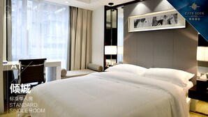 Habitación individual estándar con cama, escritorio, silla, mesita de noche, lámpara y un amplio ventanal con cortinas.