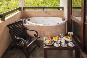 A balcony with a black wooden chair, a white bathtub, and a table set with breakfast including eggs, toast, fruit, and beverages.