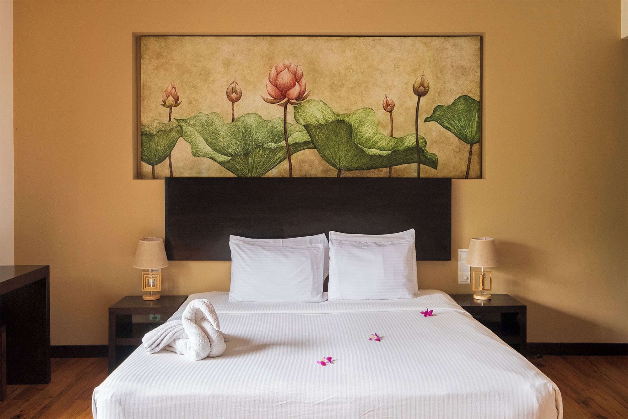 Een hotelkamer met een groot bed, twee nachtkastjes en een aan de muur hangend schilderij van lotusbloemen.
