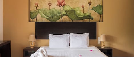 A hotel room with a large bed, two bedside tables, and a wall-mounted painting of lotus flowers.