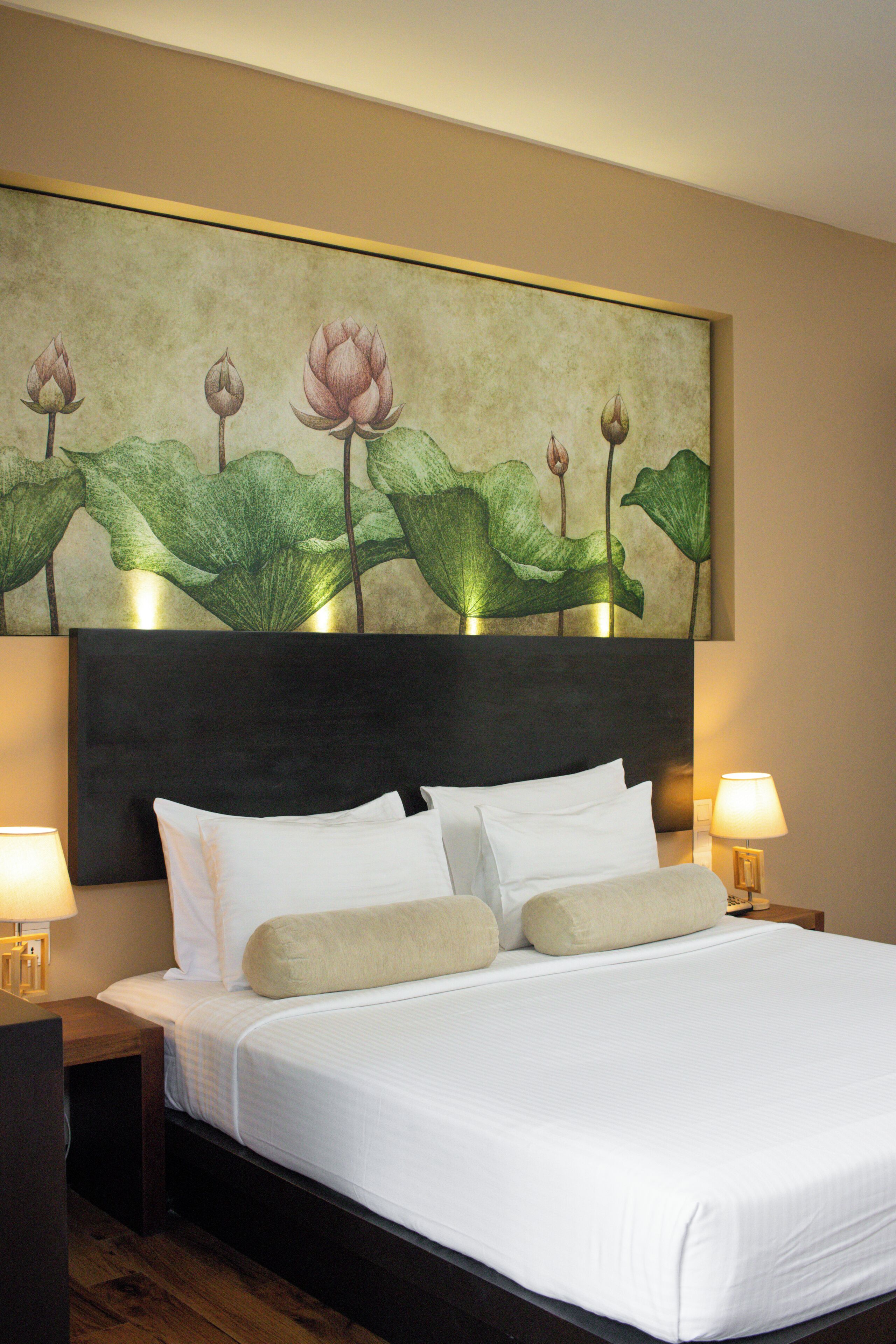 Una habitación de hotel con una cama grande, dos mesitas de noche con lámparas y un cuadro colgado en la pared con flores de loto.