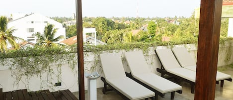 A covered outdoor seating area with lounge chairs and a wooden table, overlooking a residential neighborhood.