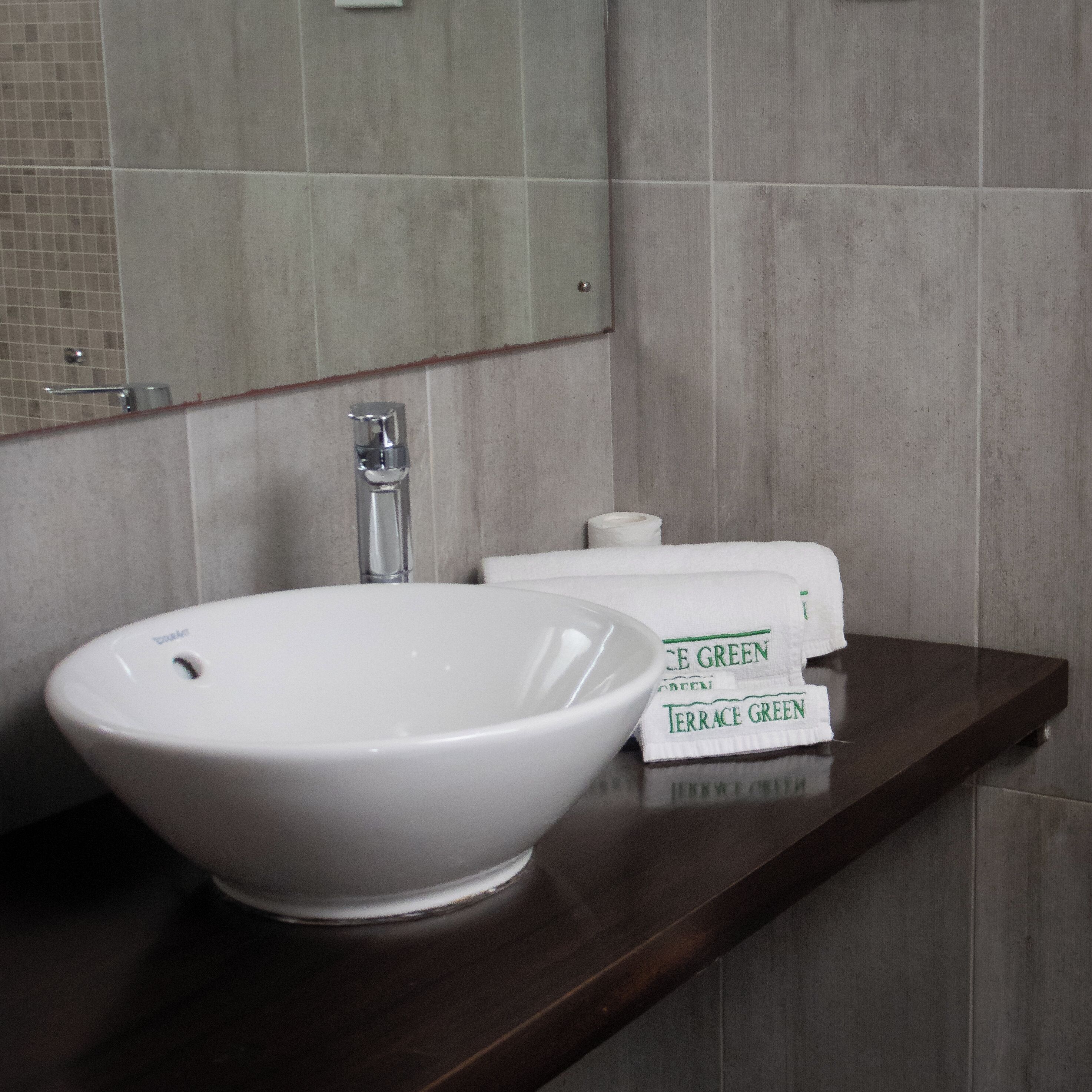 A bathroom with a white vessel sink, a mirror, and a shelf with toiletries.