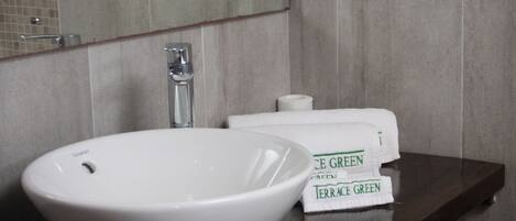 A bathroom with a white vessel sink, a mirror, and a shelf with toiletries.