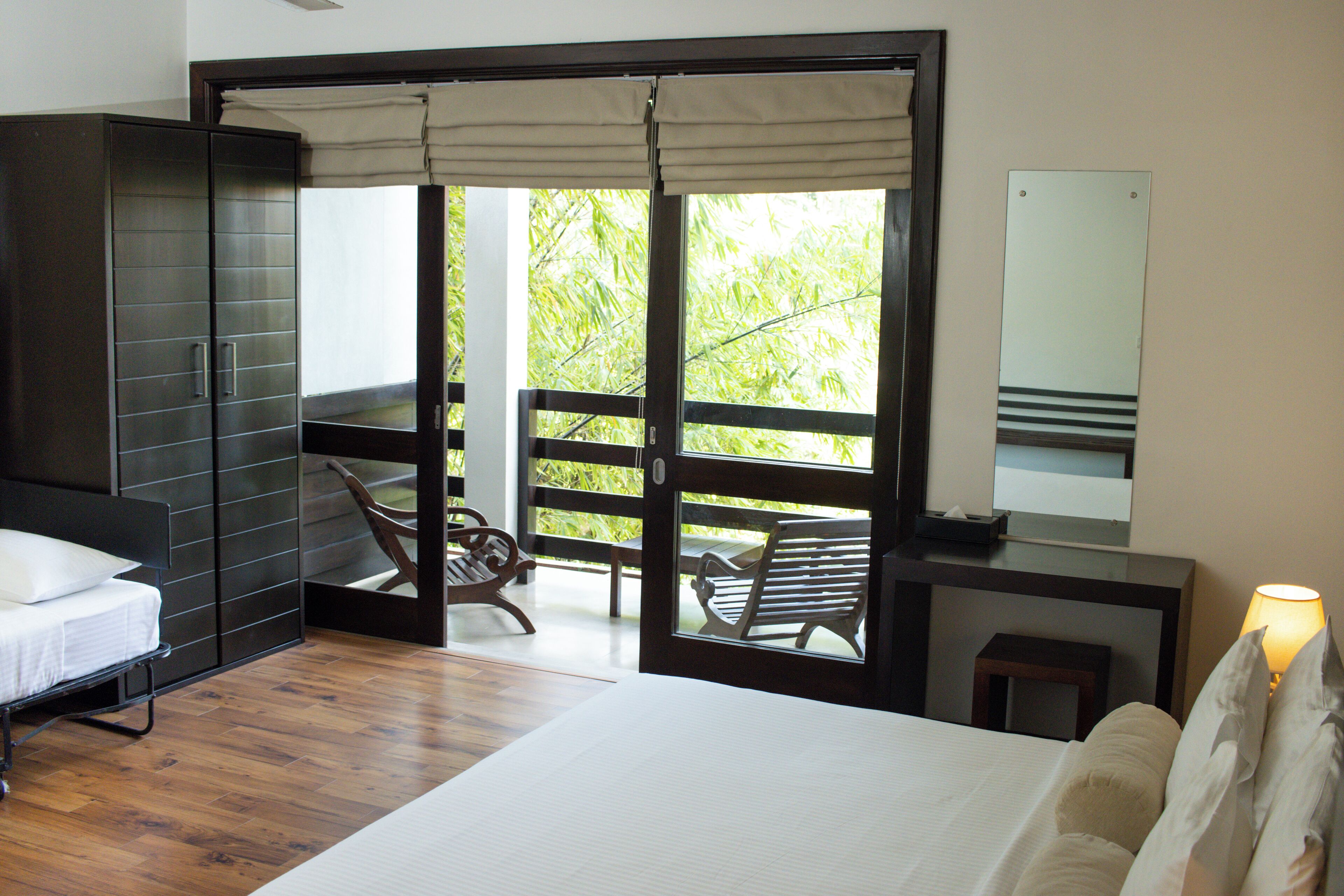 A bedroom with a bed, a wardrobe, a desk with a lamp, and a balcony with a chair.