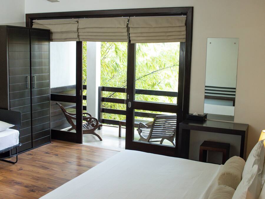 A bedroom with a bed, a wardrobe, a desk with a lamp, and a balcony with a chair.