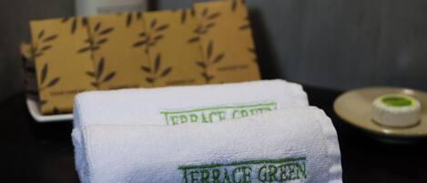 A neatly folded towel with "Terrace Green" embroidered on it, placed on a dark surface with a patterned box and a small container in the background.