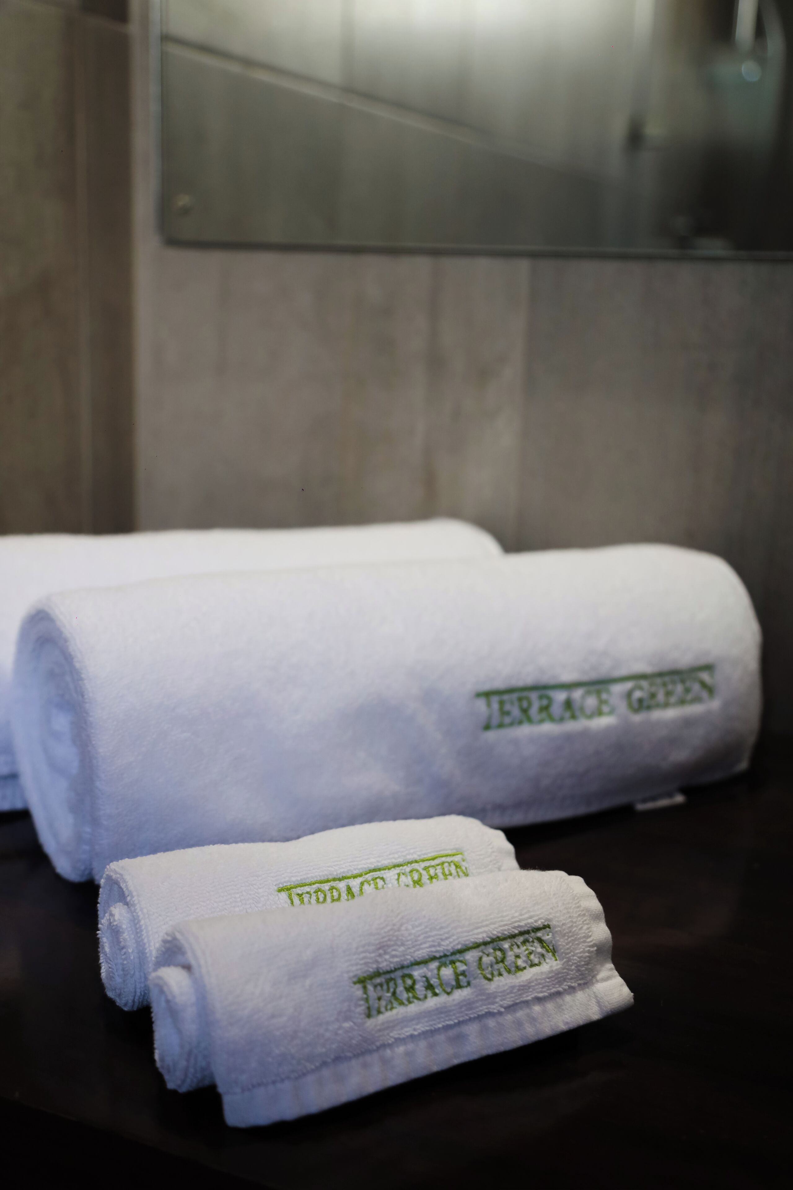 Two rolled towels with the text "Terrace Green" on them, placed on a dark surface.