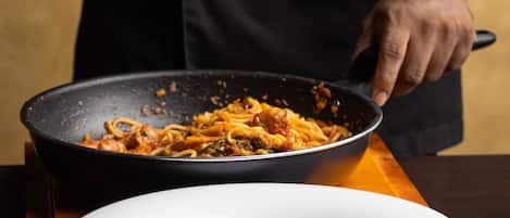 A person serving pasta from a pan to a white plate.