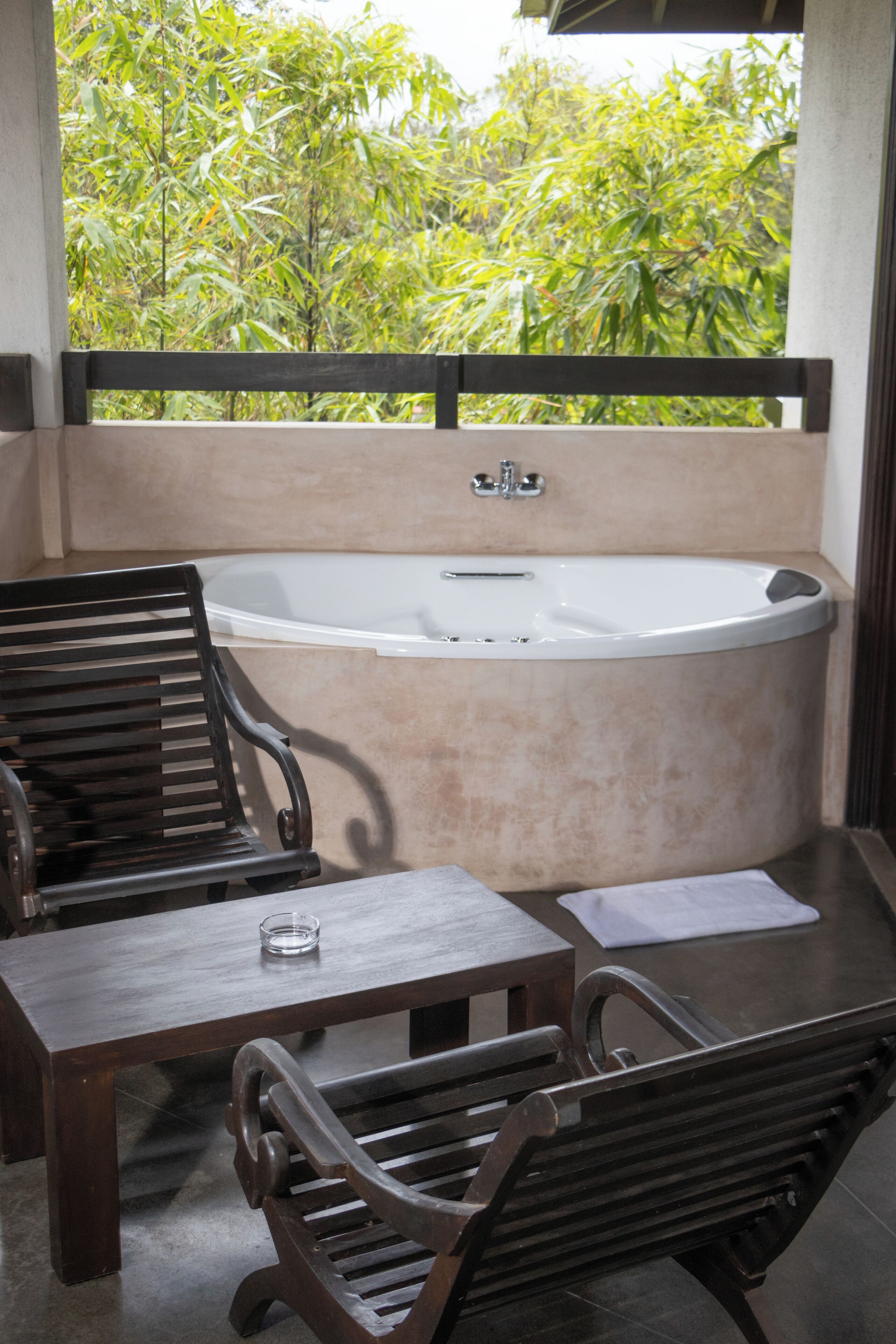 Un balcon avec une table et des chaises en bois, une baignoire et une vue sur la verdure.