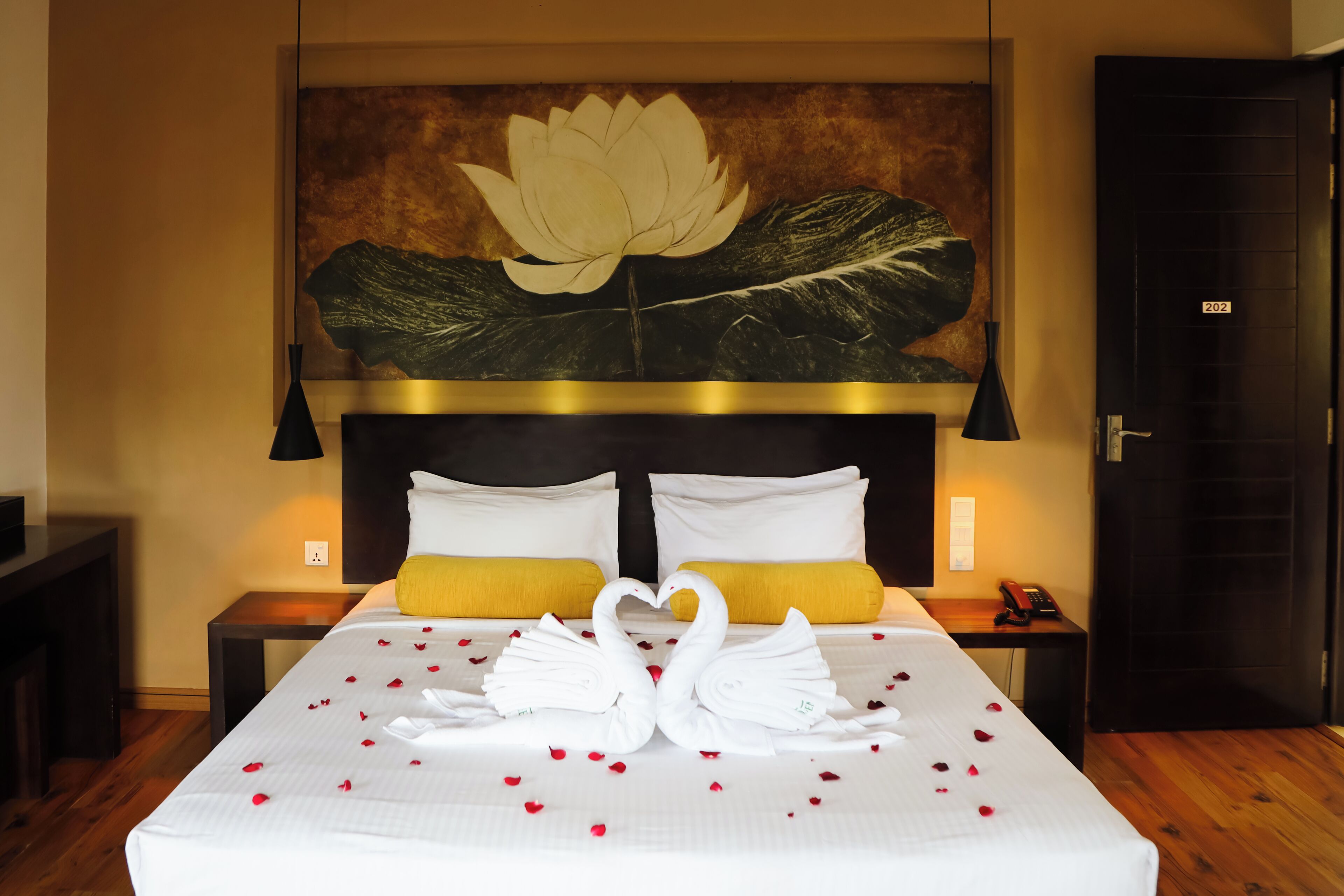 Una habitación de hotel con una cama, una gran obra de arte floral en la pared, suelo de madera y una puerta con un número.