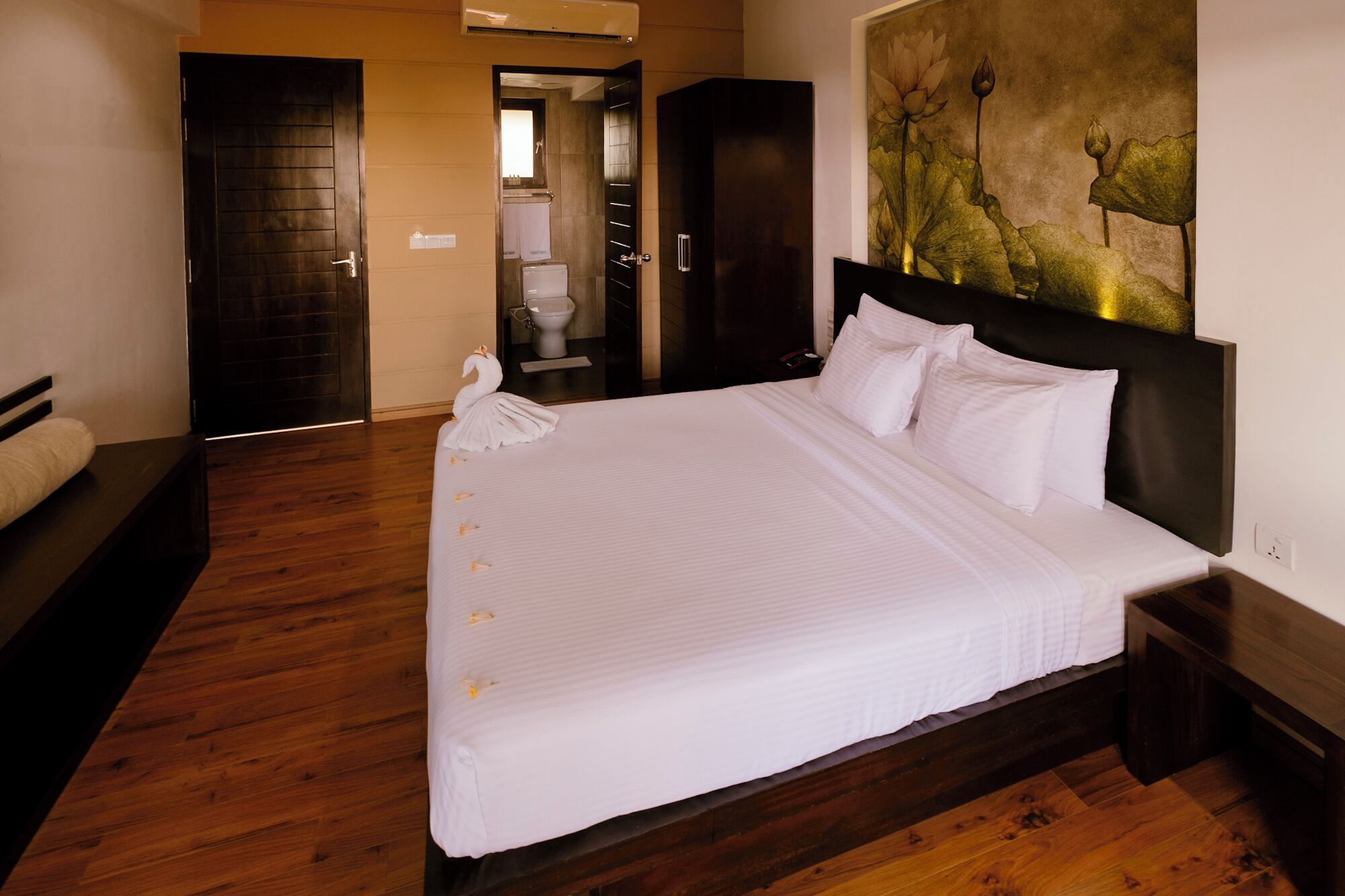 Una cama grande con sábanas blancas, un cabecero oscuro y suelo de madera.