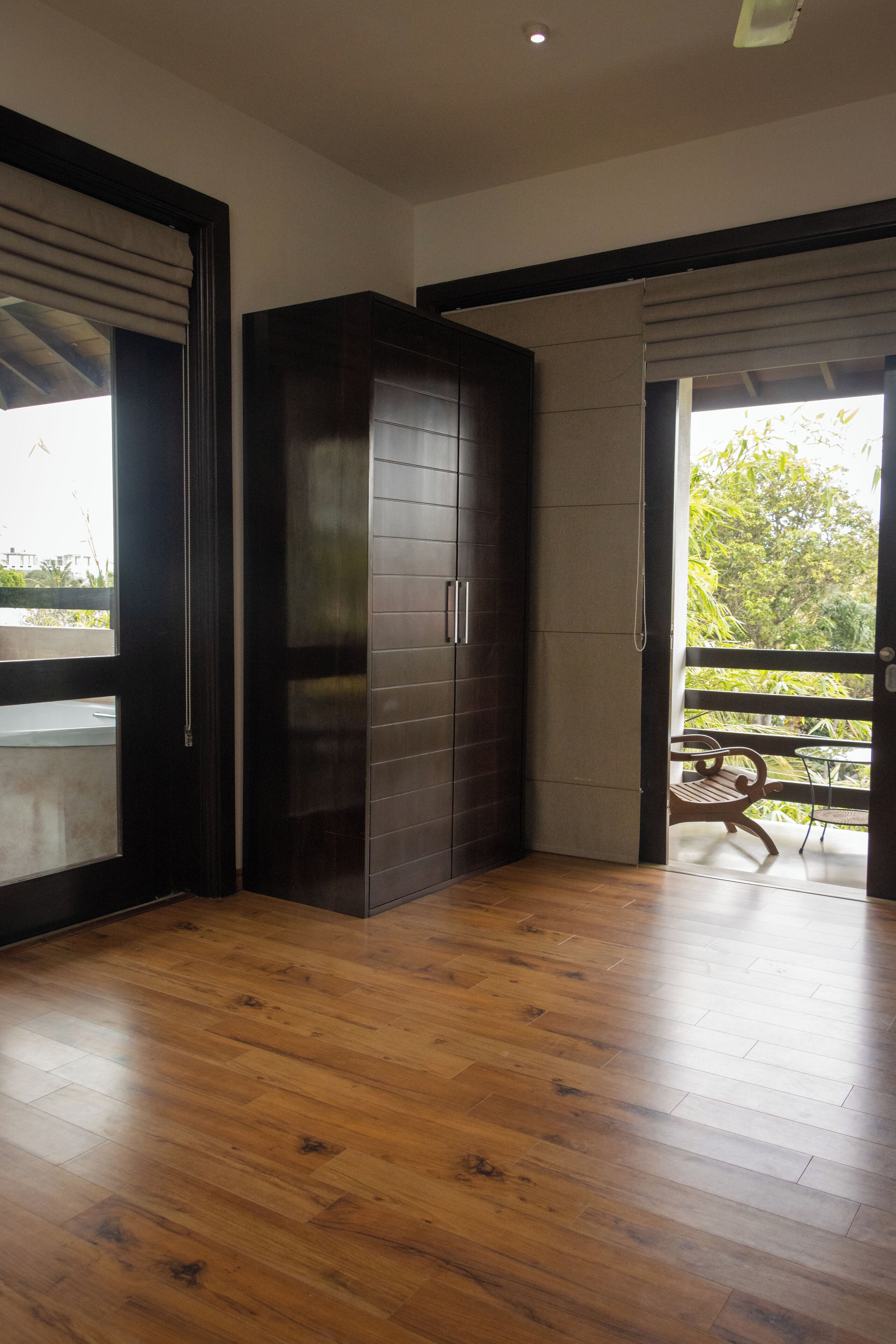 A room with a wooden floor, a dark-colored wardrobe, and a sliding glass door leading to an outdoor area with a bench.