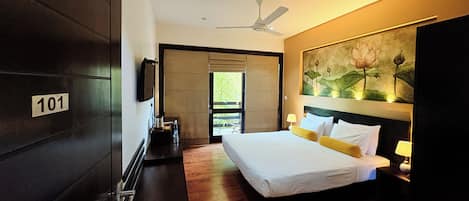 A modern hotel room with a large bed, a ceiling fan, a painting of lotus flowers, and a number sign on the door.