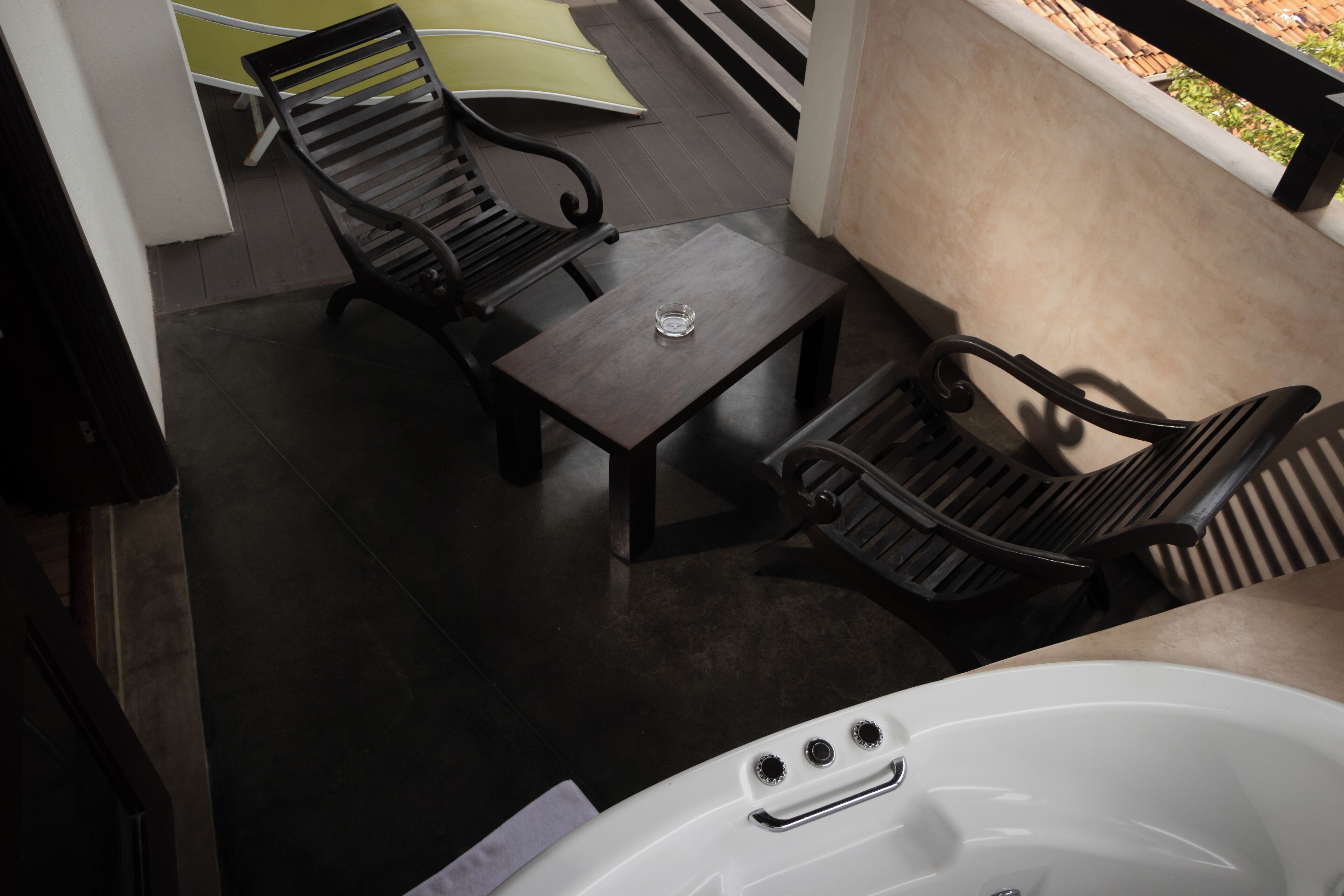 A balcony with two wooden chairs and a small table, a white bathtub, and a green mat.