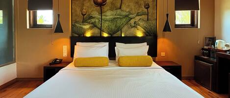 A hotel room with a large bed, two bedside tables, a nightstand, a desk with a chair, and a painting of flowers on the wall.