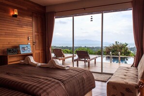 A bedroom with a large bed, a sofa, and a view of a pool and mountains.
