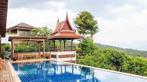 A swimming pool with a wooden deck, a gazebo, and a view of a lush green landscape.