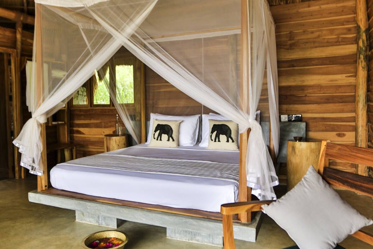 Ein Schlafzimmer einer Holzhütte mit einem Himmelbett, zwei Kissen mit Elefantenmotiv und einem Moskitonetz.