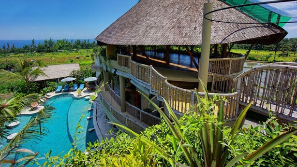A multi-story resort with a swimming pool, outdoor seating, and a view of the ocean.
