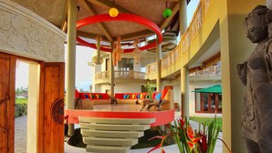 A multi-level hotel lobby with a central circular seating area, a statue, and a view of the outdoors.