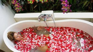 A person in a bathtub filled with water and red and white flowers.
