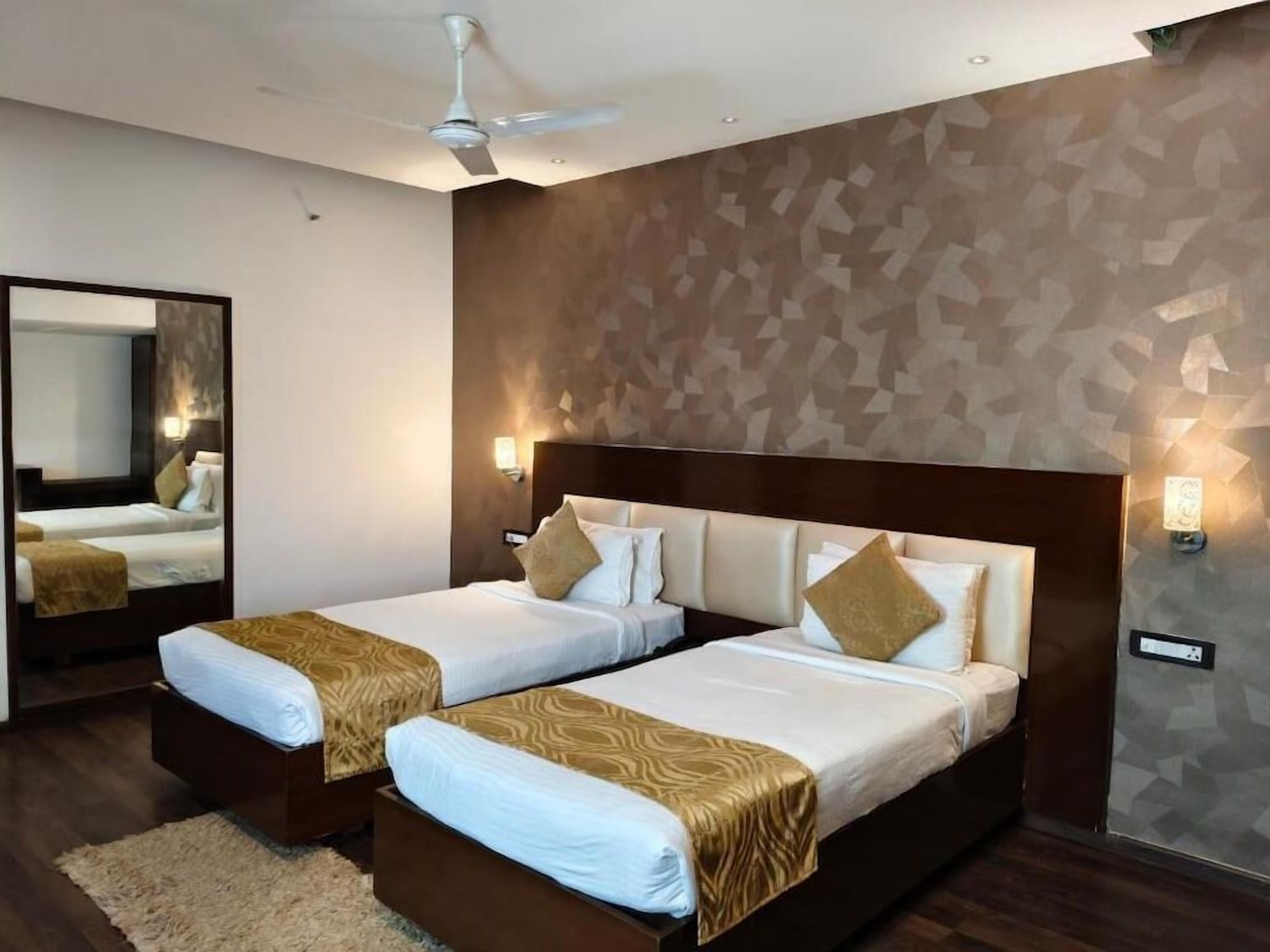 A hotel room with two beds, a ceiling fan, a large mirror, and a geometric-patterned wall.