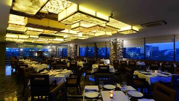 A restaurant with multiple tables set for dining, large windows offering city views, and a modern ceiling design.