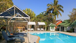 A swimming pool with lounge chairs and a covered seating area, surrounded by palm trees and buildings with green roofs. - Silamanee Resort and Spa Hotel (Mae Sai)